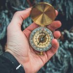 A close-up shot of a hand holding a vintage compass against a natural background.
